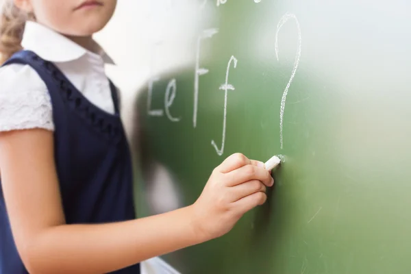 Schoolgirl writes English alphabet with chalk on blackboard — стокове фото