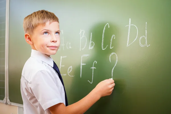 School boy scrive l'alfabeto inglese con gesso sulla lavagna — Foto Stock