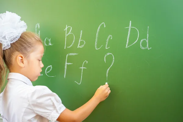 Schoolgirl writes English alphabet with chalk on blackboard — Stock Photo, Image