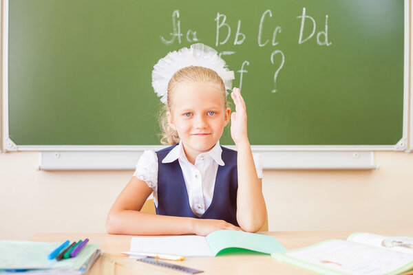 Schoolgirl sitting at desk, school classroom, on background of board