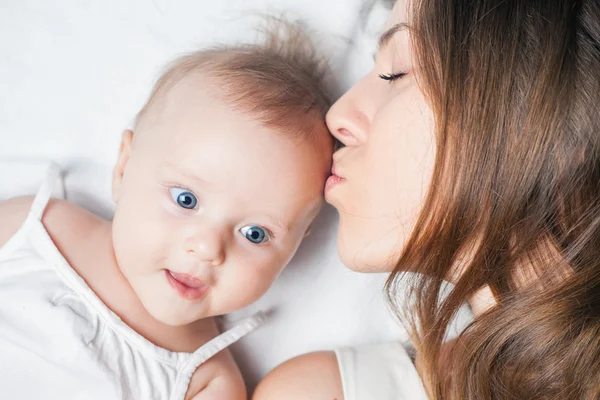 Happy mother with a baby lying on a white bed — Stock Photo, Image