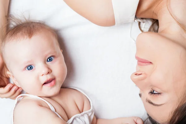 Happy mother with a baby lying on a white bed — Stock Photo, Image