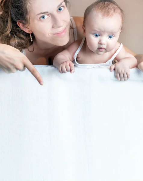 Mother with baby lying on white blanket and pointing down