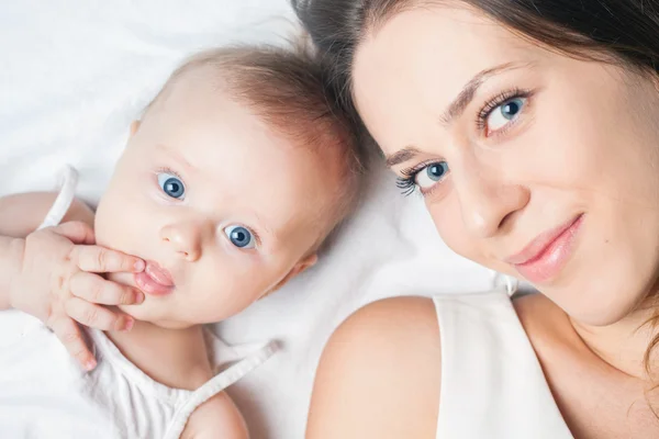 Happy mother with a baby lying on a white bed — Stock Photo, Image