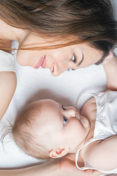 Happy mother with a baby lying on a white bed — Stockfoto