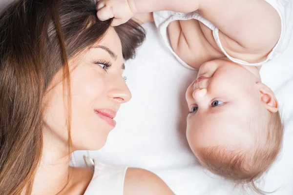 Happy mother with a baby lying on a white bed — 图库照片