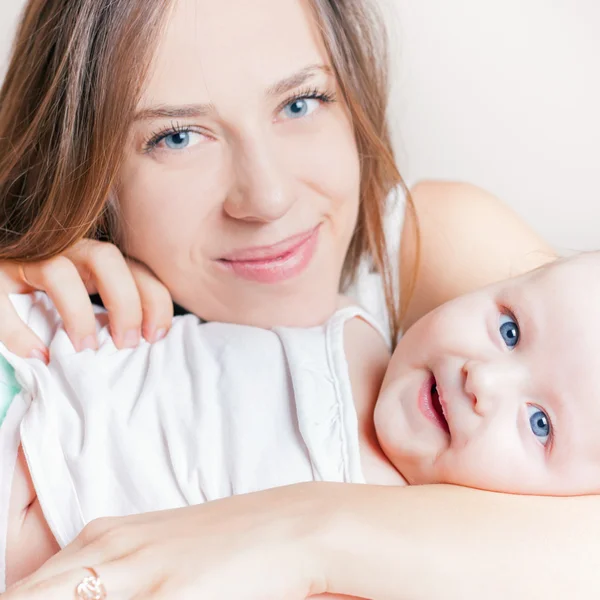 Happy mother with a baby lying on a white bed — Stock Photo, Image