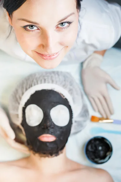 Professional woman, cosmetologist in spa salon applying mud face mask — Stock Photo, Image