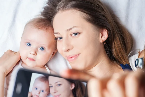 Funny baby girl with mom make selfie on mobile phone — Stock fotografie