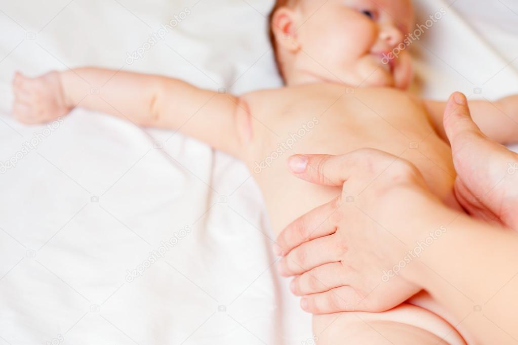 Mother makes baby massage with happy newborn at white bed