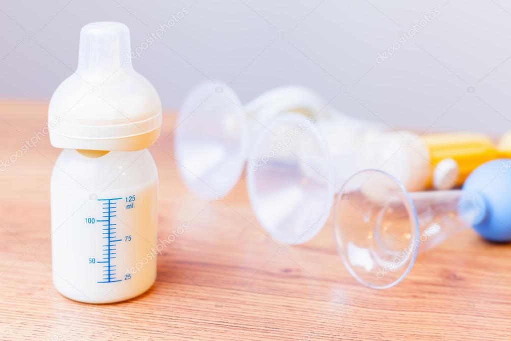 Baby bottle with milk and manual breast pump at background