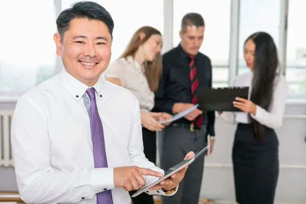 Výkonné asijské šéf pomocí tablet pc s jeho obchodní tým — Stock fotografie