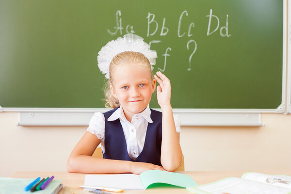 Schoolgirl sitting at desk, school classroom, on background of board