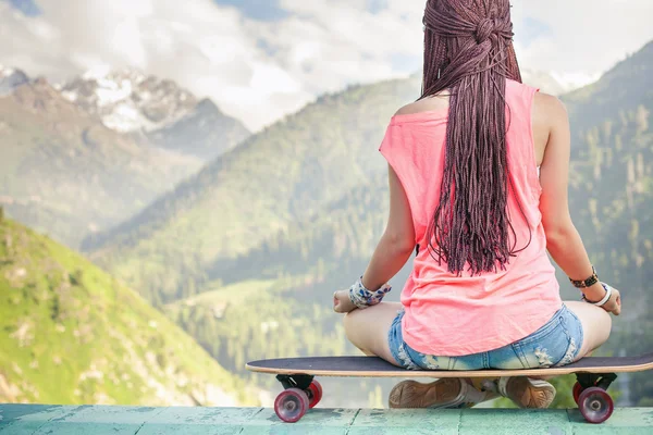 Hipster ragazza di moda che fa yoga, relax su skateboard in montagna — Foto Stock