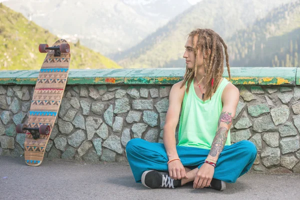 Ritratto di uomo bello fresco e divertente con skateboard in montagna — Foto Stock