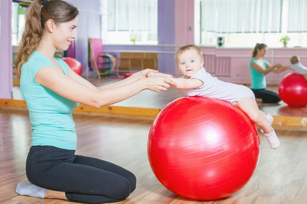 Mutter mit glücklichem Baby macht Übungen mit Gymnastikball Stockbild