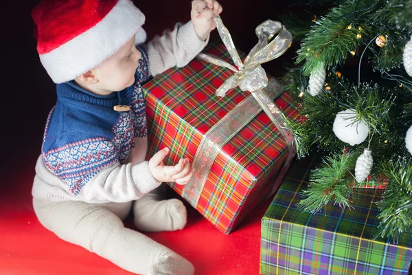 Christmas holiday. Baby in Santa hat opening box of gifts Royalty Free Stock Photos