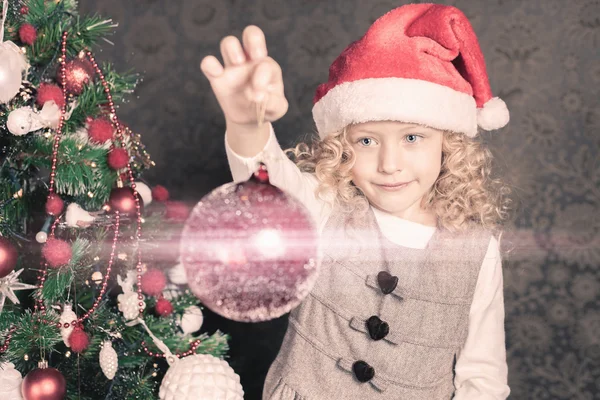 Menina engraçada decorando uma árvore de Natal e segurando bola — Fotografia de Stock