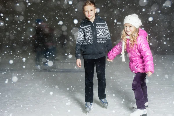 De gelukkige kinderen schaatsen op de ijsbaan, op winternacht — Stockfoto