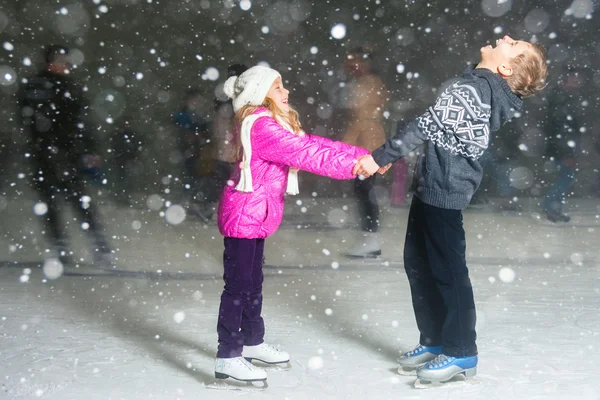 Crianças felizes patinação no gelo na pista de gelo, noite de inverno — Fotografia de Stock