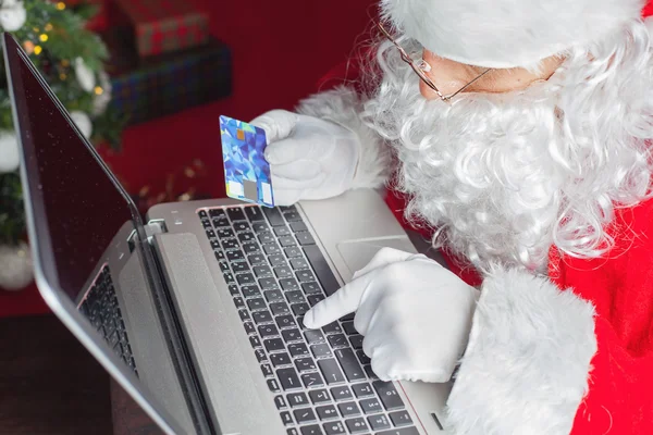 Papai Noel usando computador portátil, comprando por cartão de plástico presente de Natal — Fotografia de Stock