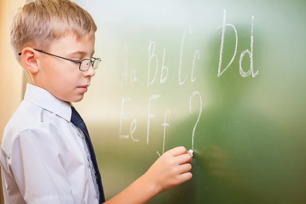 School jongen schrijft Engelse alfabet met krijt op blackboard — Stockfoto