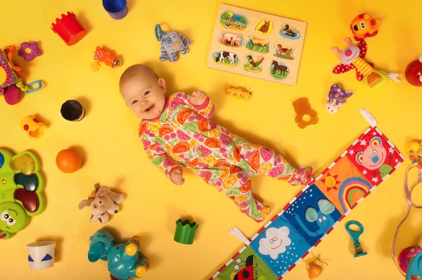 Glimlachende baby met speelgoed op een gele grond Stockafbeelding