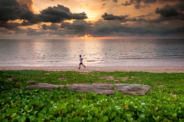 Pôr do sol atrás da praia com o homem correndo em primeiro plano — Fotografia de Stock