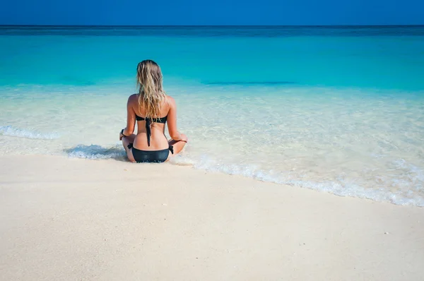 Kvinna med en svart bikini sitter och koppla av på stranden — Stockfoto