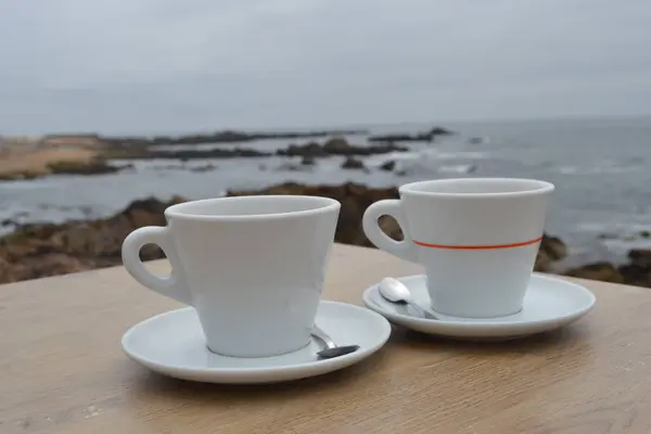 Atlantik Okyanusu 'nun arka planında çay tabağı olan iki bardak sıcak içecek.