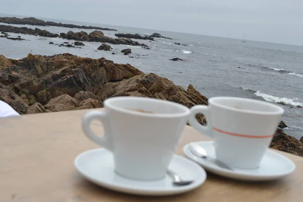 Atlantik Okyanusu 'nun arka planında çay tabağı olan iki bardak sıcak içecek.