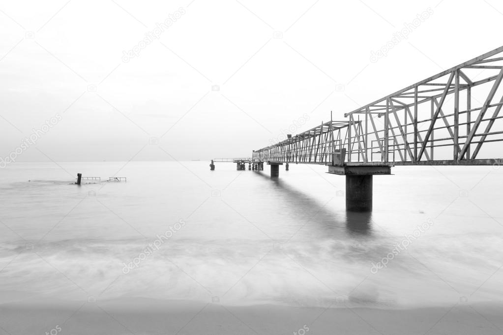 Black and white long exposure photo of steel jetty leading to the ocean.
