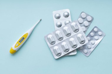 Tıbbi termometre ve su toplayan haplar beyaz arka planda. Hastalık önleme ve tedavi konsepti. Üst görünüm.