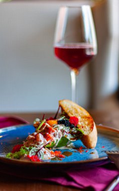 Mavi tabakta salata ve bir bardak kırmızı şarap.