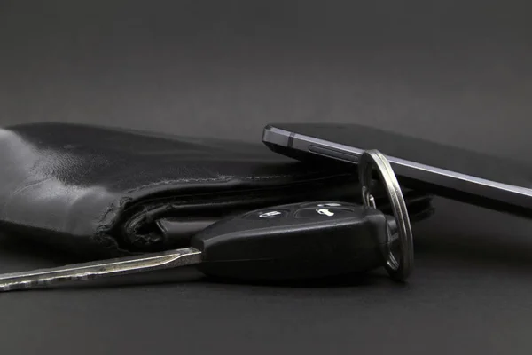 Cüzdan, telefon ve araba anahtarları koyu bir arka planda.