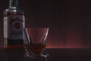 Bir bardak burbon ve bir şişe Jim Beam. Yumuşak odaklanma. Riga, Letonya - 19 Mar 2021