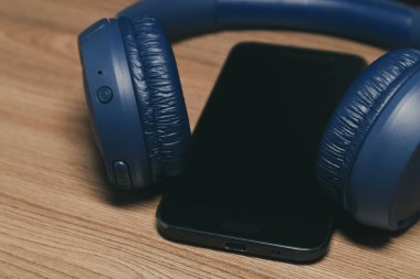 Mavi bluetooth kulaklık ve ahşap bir masada akıllı telefon.