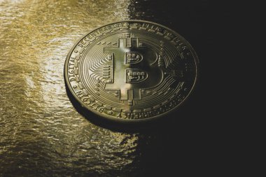 Bitcoin coin on a gold background, half light, half shadow.