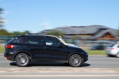 Hızlı hareket eden siyah Porsche Cayenne. Hareket bulanıklığı. Riga, Letonya - 14 Haziran 2021.