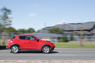 Kırmızı Nissan Juke 'un yan görüntüsü. Hareket bulanıklığı. Riga, Letonya - 15 Haziran 2021.