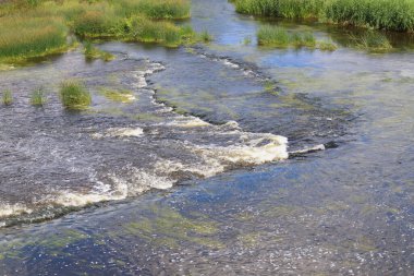Küçük şelaleleri olan sığ, geniş bir nehir manzarası.