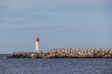 large concrete tetrapods forming a breakwater in the sea with a small lighthouse in the background. coastal protection structure against waves and erosion