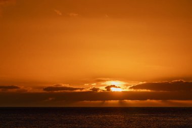 Okyanusun üzerinde altın gün batımı, güneş karanlık bulutların arkasında batıyor ve sıcak turuncu ışık gökyüzüne ve suya yayılıyor. Madeira, Portekiz 'de gün batımı.