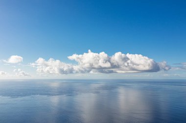 Okyanusun üzerindeki bulutlar. Büyük beyaz bulutlar berrak bir gökyüzünün altında sakin mavi bir okyanusun üzerinde sürükleniyor..
