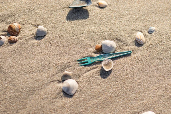 Plajı kirleten deniz kabukları arasında mavi plastik çatal (Kijkduin, Lahey, Hollanda)
