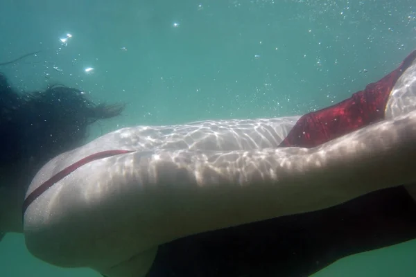 Woman swimming underwater in the sea in a red swimsuit. Young female swimmer swimming underwater.