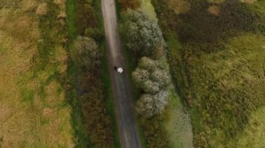 Genç bir çift, erkek ve kadın toprak bir yolda yürüyor tarlalar ve bataklıklar arasında.