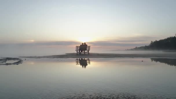 Pareja en el amor sentado en un banco en el centro del lago y cumplir con el amanecer. — Vídeos de Stock