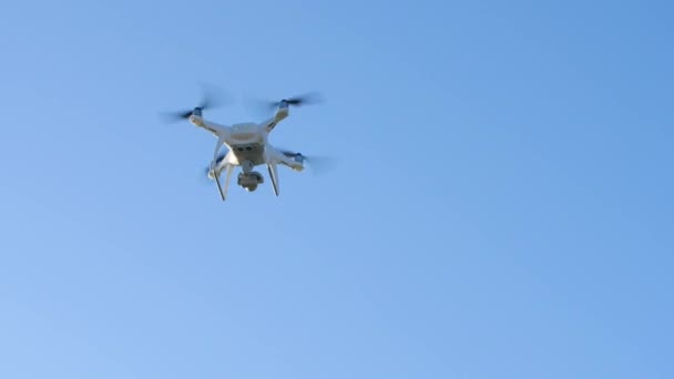 Um quadricóptero branco aparece em um fundo de céu azul e voa para longe. — Vídeo de Stock