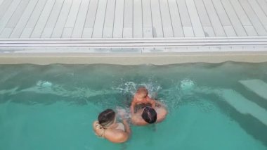 Çocuk havuza yaklaştı ve suya atladı. Babam topu yakalıyor ve neşeyle üzerine atıyor. Annem mutlu bir anda seviniyor. Aile zamanı. Aktif ebeveynlik.